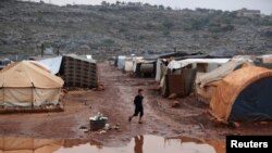 FILE - An internally displaced Syrian boy walks through mud near the tents after heavy rain at Kafr Arouk camp in Idlib, Syria, Dec. 20, 2021. 