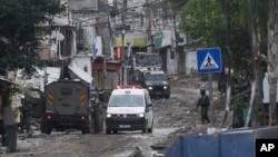 FILE - A Red Crescent ambulance passes by Israeli troops during an army raid in the Tulkarem refugee camp, West Bank, Jan.17, 2024.
