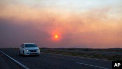 A car rides on the road to Roswell, New Mexico, as smoke from a wildfire partially blocks the sun near the village of Ruidoso, June 18, 2024.