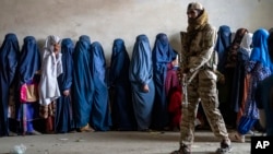 FILE - A Taliban fighter stands guard as women wait to receive food rations distributed by a humanitarian aid group, in Kabul, Afghanistan, May 23, 2023. 