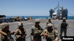 FILE - U.S. soldiers stand at Trident Pier, a temporary pier to deliver aid, off the Gaza Strip, amid the ongoing conflict between Israel and Hamas, near the Gaza coast, June 25, 2024, as an aid truck drives off a ship in the background.