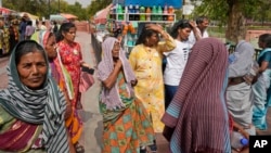 People cover their heads to shield from the heat as they buy water bottles in New Delhi, India, Tuesday, June 18, 2024.