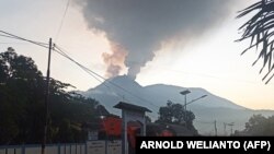 Pengendara berkendara saat Gunung Lewotobi Laki-Laki mengeluarkan asap panas di Flores Timur, Nusa Tenggara, Timur, 2 Januari 2024. (Foto: AFP/ARNOLD WELIANTO)