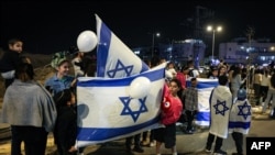 People hold flags of Israel and cheer after a vehicle carrying hostages released by Hamas passed towards an army base in Ofakim, southern Israel, on Nov. 26, 2023, after hostages were released by Hamas from the Gaza Strip.
