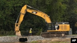 FILE - A worker examines repairs to a dam that had been opened up during recent flooding at Barrett Park, Sept. 13, 2023, in Leominster, Mass.