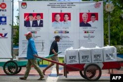Petugas membawa kotak suara melewati poster calon pemilu setelah diangkut dengan perahu motor ke Kepulauan Seribu di Jakarta, 9 Februari 2024, menjelang pemilihan presiden dan legislatif Indonesia yang dijadwalkan digelar pada 14 Februari. (BAY ISMOYO / AFP)