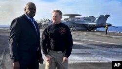 Defense Secretary Lloyd Austin, left, talks with the commanding officer of the USS Gerald R. Ford, Navy Capt. Rick Burgess, during an unannounced visit to the ship on Dec. 20, 2023. 