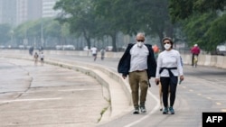 People walk along the shoreline of Lake Michigan with heavy smoke from the Canadian wildfires in the background, on June 27, 2023, in Chicago.