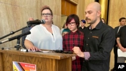 Parents Devon and Robert Dolney, of Fargo, ND, stand with their 12-year-old, Tate, during a press conference, Sept. 14, 2023, at the state Capitol in Bismarck, ND. 