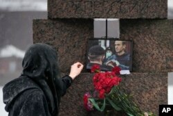 สตรีผู้หนึ่งวางดอกไม้และแตะที่ภาพของอเล็กเซ นาวาลนี ผู้ล่วงลับ เมื่อวันที่ 17 ก.พ. 2024