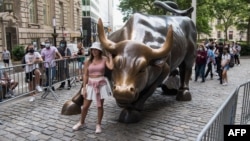 资料照：游客与纽约曼哈顿的华尔街铜牛合影。（2021年6月18日）