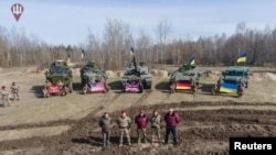 Ukrainian defense officials pose in front of foreign-supplied military hardware, including a British Challenger 2 battle tank, at an unidentified location in Ukraine, in this handout picture released by Ukraine's Defense Ministry March 27, 2023.