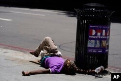 A homeless person lies on the sidewalk while holding a water bottle, Sunday, July 2, 2023, in downtown Los Angeles.