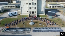 In this photo from the Defense Advanced Research Projects Agency, drones and participants in a Defense Department urban warfare exercise pose at Fort Campbell, Tenn., on Nov., 2021. A single operator supervised a swarm of more than 100 drones at the exercise. (DARPA via AP)