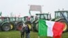 Bendera nasional Italia berkibar di depan traktor yang diparkir di sepanjang jalan saat para petani melakukan aksi protes di dekat pintu masuk jalan raya di Melegnano, dekat Milan, 30 Januari 2023. (GABRIEL BOUYS / AFP)