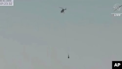 This image taken from video provided by NASA TV shows the capsule released by the Osiris-Rex spacecraft being lifted off by a helicopter after landing to Earth at Dugway Proving Ground, Utah, Sept. 24 2023. (NASA TV via AP)