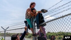 FILE - Migrants climb over a barbed wire fence after crossing the Rio Grande into US from Mexico, in Eagle Pass, Texas, Aug. 25, 2023. 
