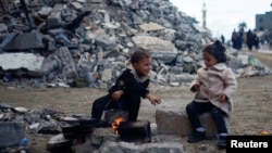Dua anak Palestina menghangatkan diri dekat api di samping puing-puing rumah yang hancur akibat serangan Israel di Khan Younis di Jalur Gaza selatan, 27 November 2023.