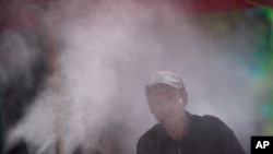 Seorang pria tampak berusaha mendinginkan badannya dengan semprotan air yang terpasang di jalanan Las Vegas, pada 4 Juni 2024. (Foto: AP/John Locher)