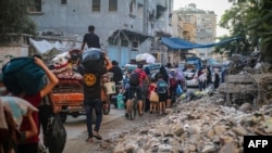 FILE - Palestinians carrrying their personal belongings flee the al-Bureij refugee camp in the central Gaza Strip on July 28, 2024. 