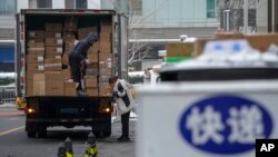 A worker unloads food products as a woman checks stock lists at a loading area outside a shopping mall in Beijing, China, Dec. 12, 2023. Chinese leaders have wrapped up a two-day annual meeting to set economic priorities for the coming year.