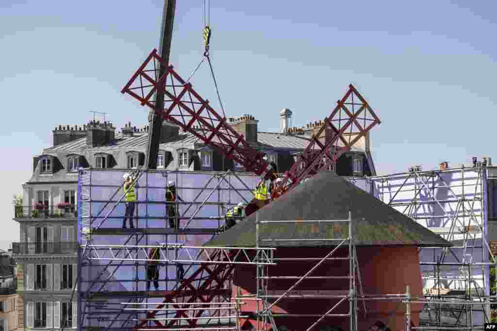 Workers install one of the four temporary windmill sails on the top of the Moulin Rouge cabaret following the collapse of the former ones, in Paris, France.