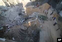 Palestinians stand by the building of the Zanon family, destroyed in Israeli airstrikes in Rafah, Gaza Strip,, Oct. 14, 2023.