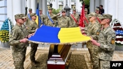 سربازان اوکراینی پرچم ملی اوکراین را برای پوشاندن تابوت داوطلب آمریکایی به نام کریستوفر جیمز کمپبل در مراسم تشییع جنازه وی در خارج از کلیسای جامع گنبد طلایی میخایلو در کی یف در دست دارند
