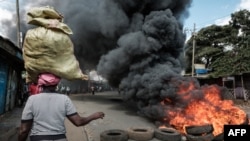 Mwanamke akiwa na mzigo kichwani wakati wa maandamano, akipita kwenye kizuizi kinachowaka moto eneo la Kibera, Nairobi, Machi 30, 2023. Picha na Yasuyoshi CHIBA / AFP.