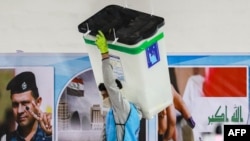 A worker of Iraq's Independent High Electoral Commission (IHEC) carries a sealed ballot box as others perform a manual count of votes to match the electronic count at one of the commission's headquarters in the Karkh district of Baghdad, Dec. 23, 2023.