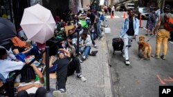 FILE - Migrants sit in a queue outside the Roosevelt Hotel, which is being used by the city as temporary housing, on July 31, 2023, in New York.