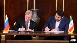 A handout photo made available by the Iranian presidential office shows Iranian Road Maintenance & Transportation Organisation Minister Mehrdad Bazrpash (R) and his Russian counterpart Vitaly Savelyev signing an agreement in Tehran, May 17, 2023.