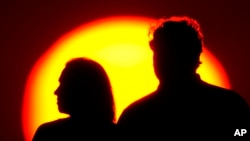 FILE - A couple watches the sun set from a park in Kansas City, Missouri, July 10, 2021.
