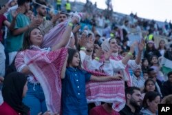 Perempuan Yordania mengenakan syal dan kaos kotak-kotak merah putih tradisional Yordania menari dan bernyanyi saat konser digelar di stadion olahraga di Amman, Yordania, Senin, 29 Mei 2023. Konser gratis ini menampilkan penyanyi Arab terkenal, termasuk bintang Mesir Tamer Hosny, menjadi bagian dari perayaan menjelang pernikahan Putra Mahkota Hussein dan tunangannya, arsitek Saudi Rajwa Alseif akhir pekan ini. (AP/Nasser Nasser)