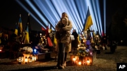 FILE - A woman and her daughter listen to a prayer for fallen soldiers at Lviv cemetery, western Ukraine, on Feb. 23, 2023.