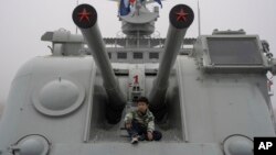 FILE - A child sits near canons on a retired warship at the Chinese People's Liberation Army Naval Museum in Qingdao in eastern China's Shandong province on April 23, 2024.