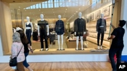A window washer cleans the display window of a clothing store as shoppers pass by, at a mall in Lone Tree, Colorado, April 29, 2024.