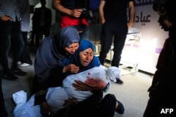 A Palestinian woman holds the shrouded body of a child killed in Israeli bombardment, at a health clinic in the area of Tel al-Sultan in Rafah in the southern Gaza Strip, May 26, 2024