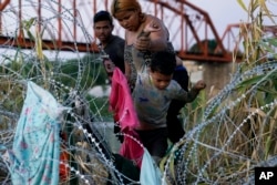 Para migran memanjat kawat berduri setelah mereka menyeberangi Rio Grande dan memasuki AS dari Meksiko, Sabtu, 23 September 2023, di Eagle Pass, Texas. (Foto AP/Eric Gay)