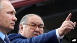 FILE - Russian businessman and close ally of President Vladimir Putin Alisher Usmanov points while speaking Putin, left, at the Lebedinsky GOK mining plant, in Gubkin, Belgorod region, Russia, July 14, 2017. (Mikhail Klimentyev, Sputnik, via AP)