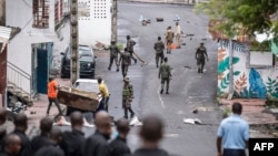 Des gens retirent un débris de la route alors que des soldats comoriens patrouillent à la suite d'une manifestation de l'opposition à Moroni le 17 janvier 2024, suite à l'annonce des élections présidentielles.