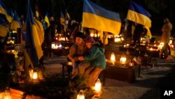 Olesia, 41, and daughter Uliana, 8, sit next to the grave of her husband, Ihor Marchenko, at Lviv cemetery, western Ukraine, on Feb. 23, 2023. 