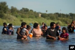 Beberapa keluarga migran Amerika Tengah berusaha menyeberangi sungai Rio Grande setelah menyeberang dari Meksiko ke AS, 1 Agustus 2023, di Eagle Pass, Texas.