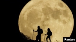 FILE - Women walk up a mountain with the full moon known as the "Sturgeon Moon" in the background, in Arguineguin, on the island of Gran Canaria, Spain, Aug. 1, 2023.