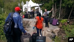 FILE - A Royal Canadian Mounted Police officer informs a migrant couple of the location of a legal border station, shortly before they illegally crossed from Champlain, N.Y., to Saint-Bernard-de-Lacolle, Quebec, using Roxham Road, Aug. 7, 2017.