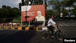 A man rides a bicycle next to a sign showing the image of Indian Prime Minister Narendra Modi, ahead of G20 Summit in New Delhi, Sept. 8, 2023.
