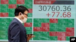 Seseorang berjalan di depan papan saham elektronik yang menunjukkan indeks Nikkei 225 Jepang di sebuah perusahaan sekuritas Kamis, 25 Mei 2023, di Tokyo. (AP/Eugene Hoshiko)