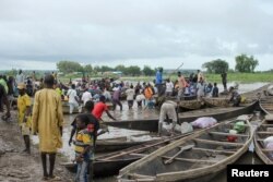 Beninese and Nigerien nationals use canoes and motorized boats to cross the Niger River in both directions as trucks carrying aid wait, due to sanctions imposed by Niger's allies, in the border town of Malanville, Benin, Aug. 17, 2023.