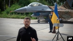 Ukraine's President Volodymyr Zelenskyy answers media questions standing against the backdrop of an F-16 fighter jet at an undisclosed location in Ukraine, Aug. 4, 2024.