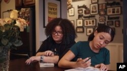 FILE - Gionna Durham, 13, left, spends time in the kitchen as her sister Grace Durham, 11, right, draws on Jan. 27, 2024, in New York.